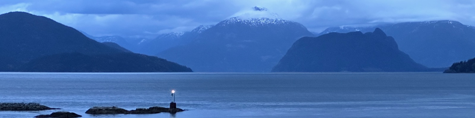 Layered coastal mountains and a small light beside the water
