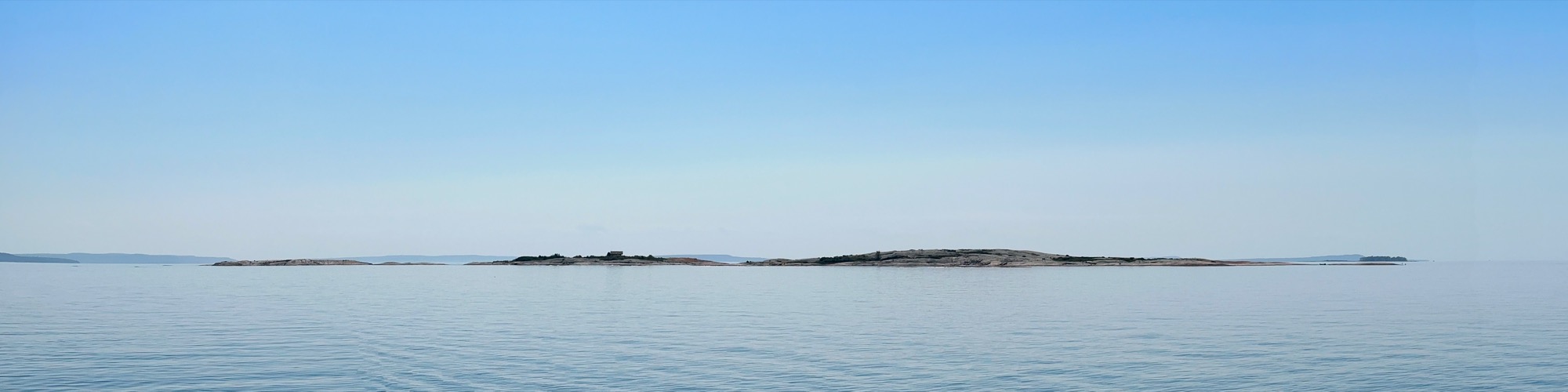 Low rocky islands across calm water beneath a clear blue sky