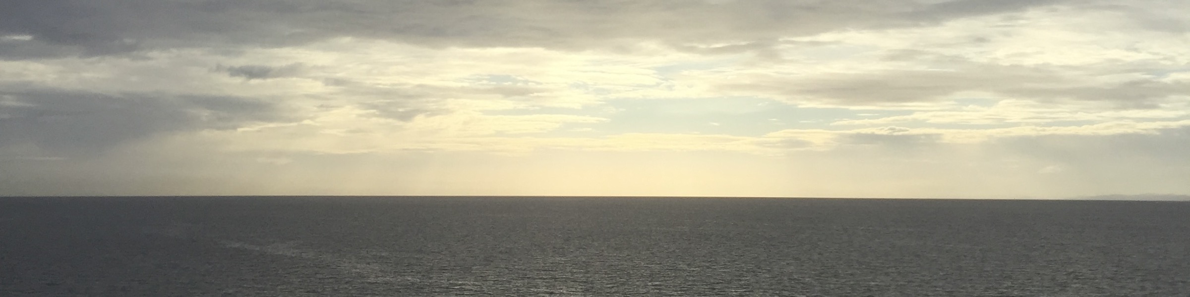 Sunlight breaking through clouds above an open sea horizon